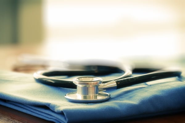 Stethoscope with blue doctor coat on wooden table with shallow DOF evenly matched and background